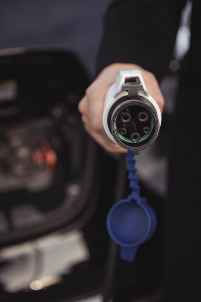 close up of man holding car charger at electric vehicle charging station